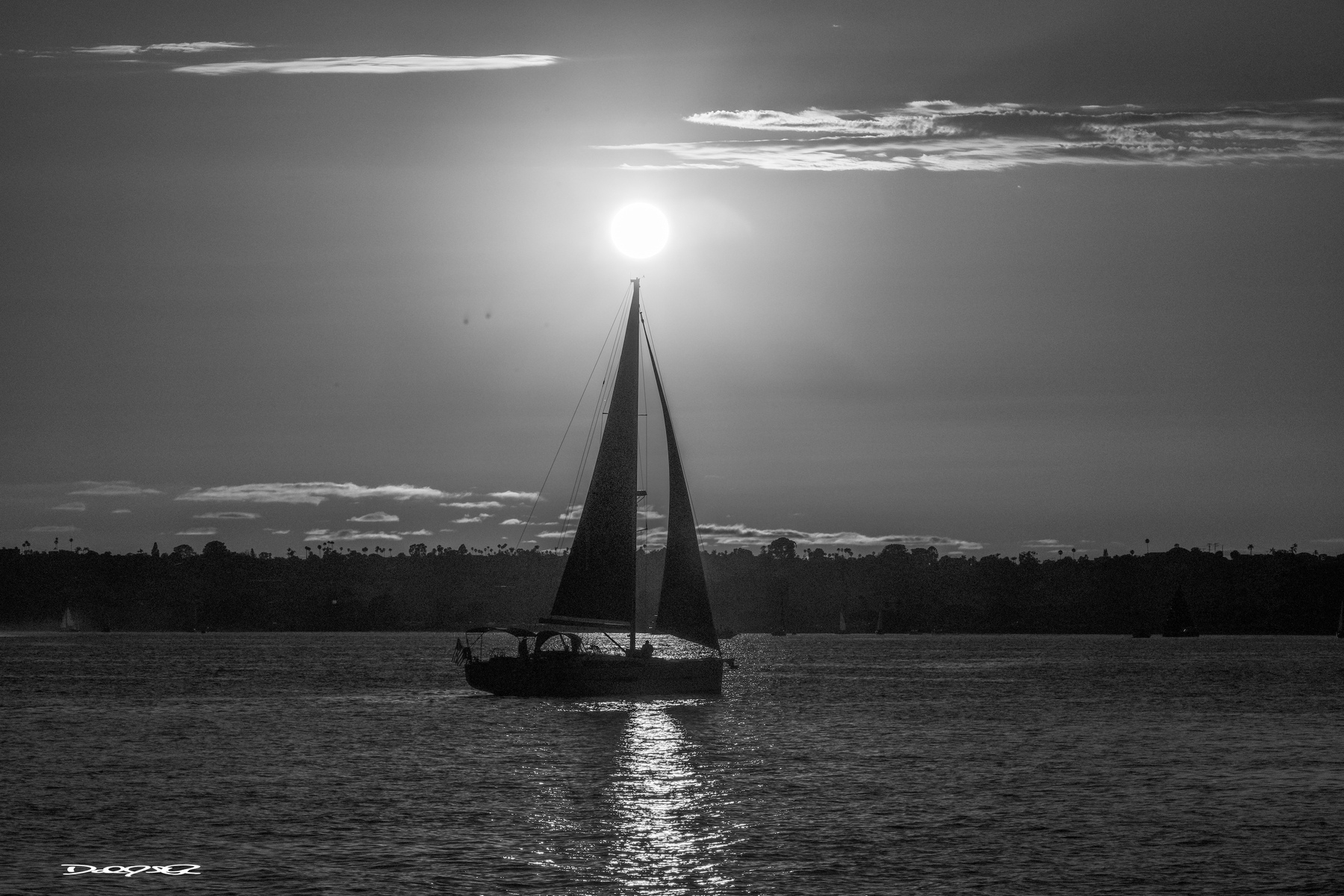 A sailboat is silhouetted against a dramatic sunset, with the sun positioned just above its mast over calm waters.