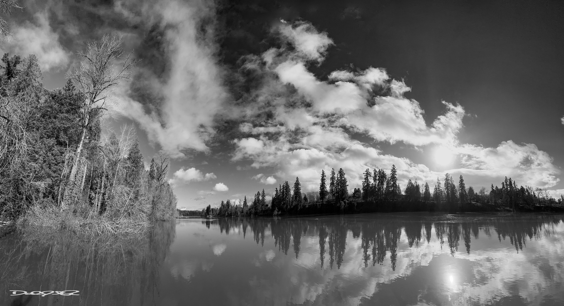 A serene landscape captures a reflective body of water surrounded by trees and a partly cloudy sky.