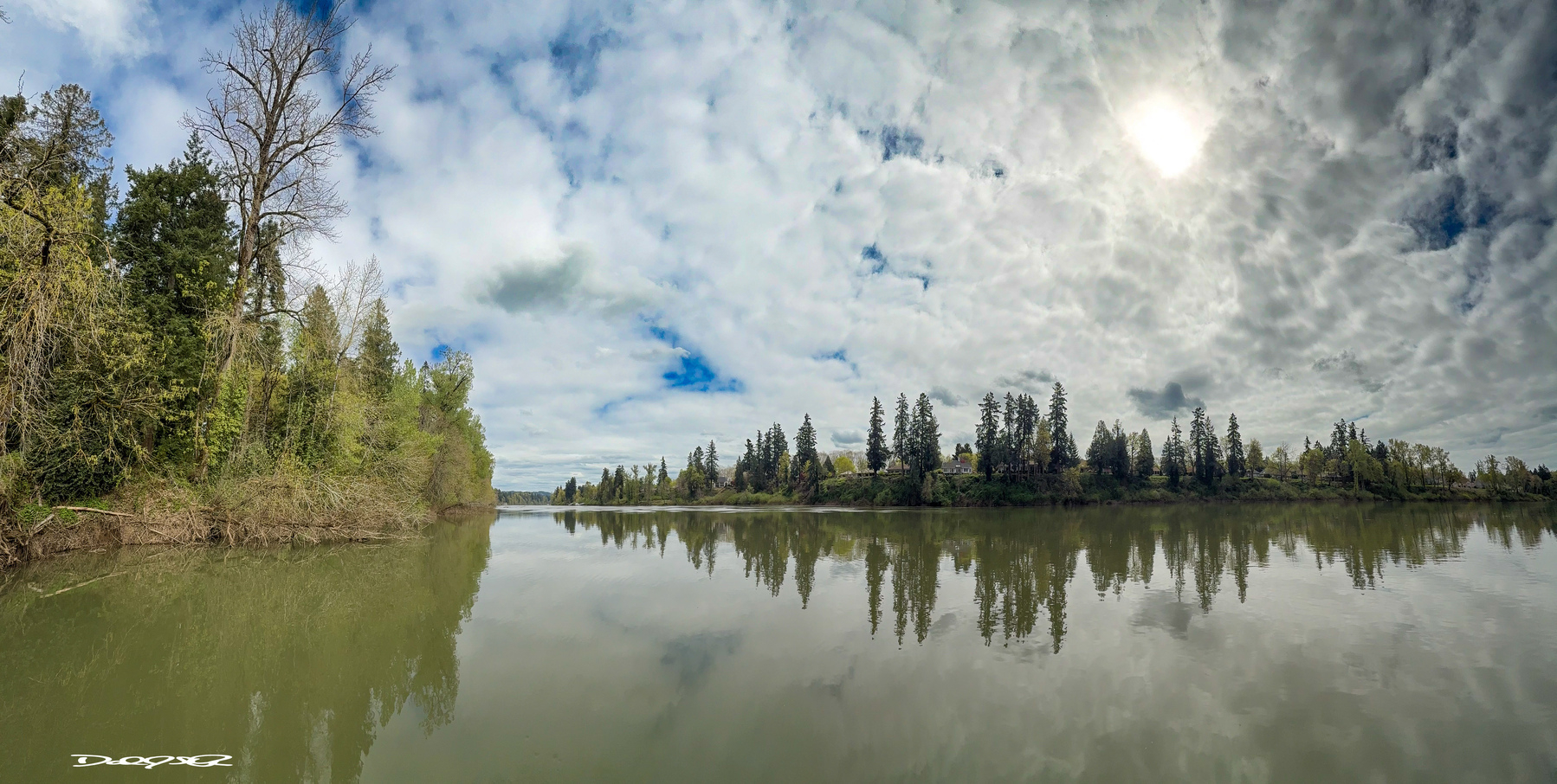 A calm Willamette River and a spring sky covered in mixed clouds