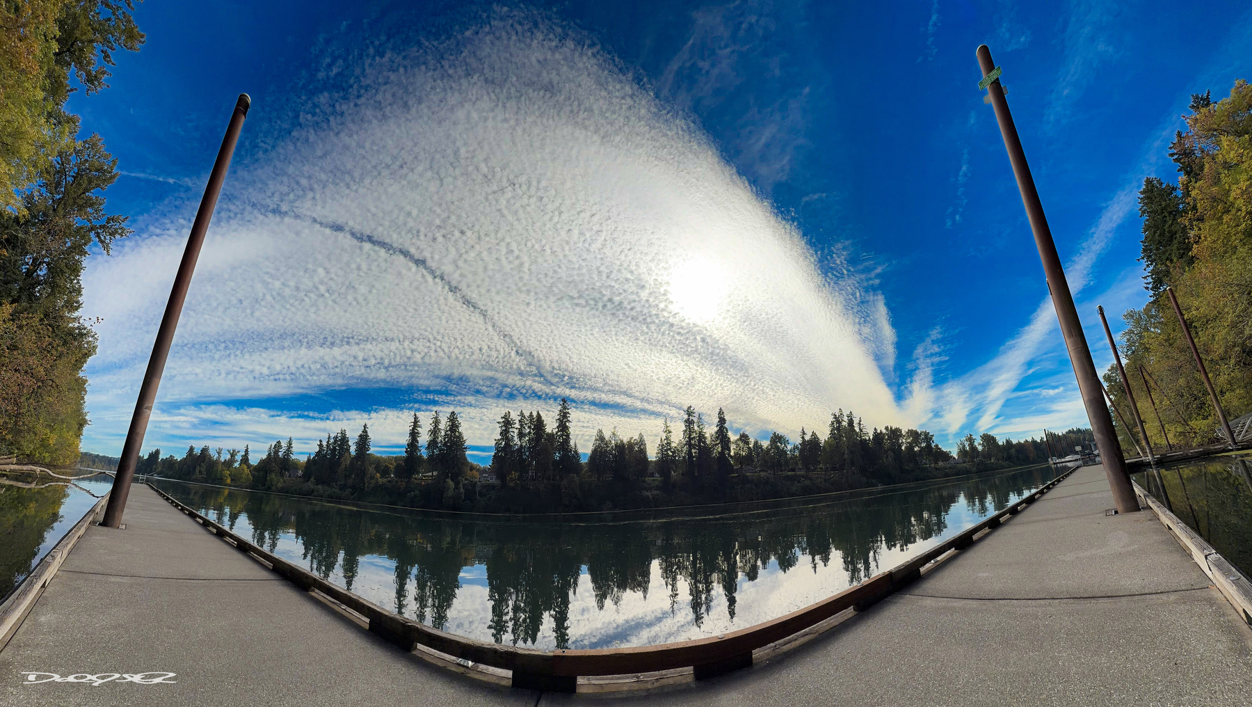 A panoramic view of a serene Willamette River is framed by two dock piers, with a dramatic sky featuring streaky clouds overhead.