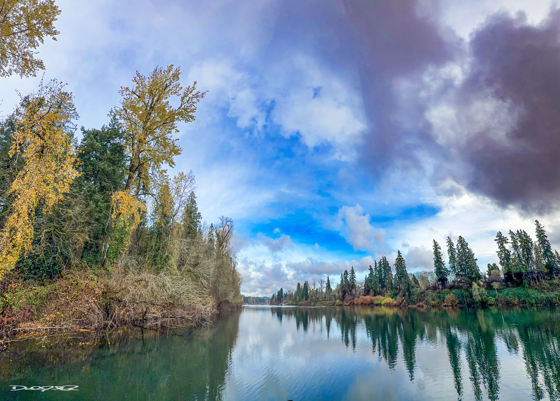 A peaceful river is surrounded by trees with a dramatic cloudy sky above.