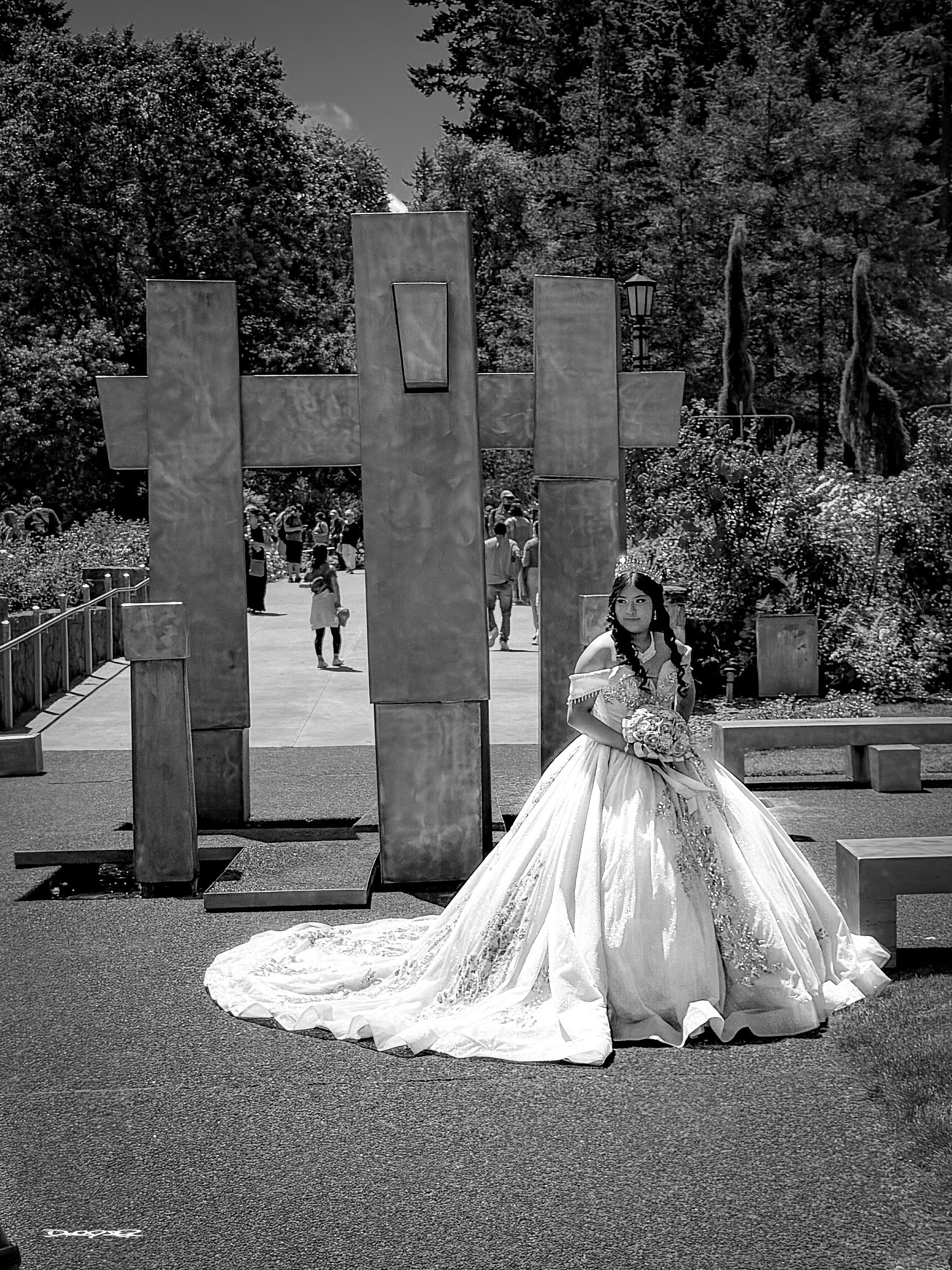 A bride in a flowing gown poses in front of a modern sculpture in an outdoor setting with trees.