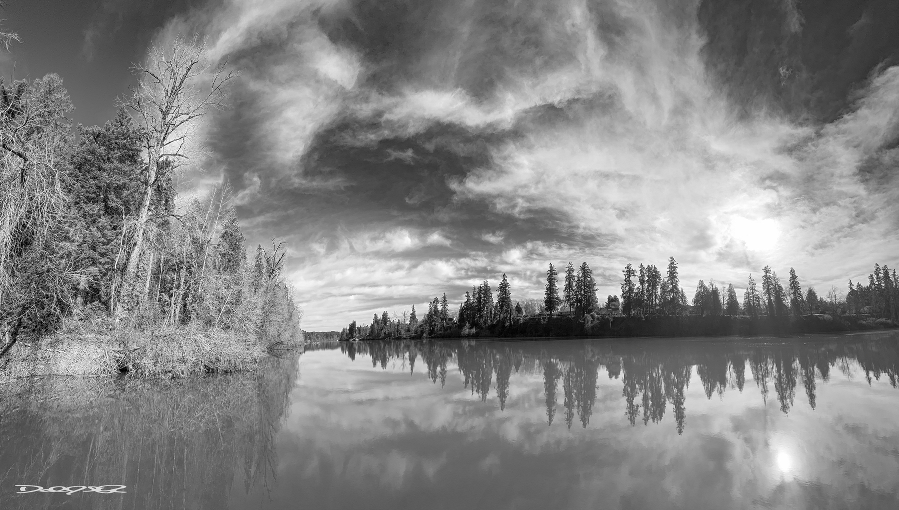 A tranquil black-and-white landscape showcases a reflective lake surrounded by trees under a dramatic sky.